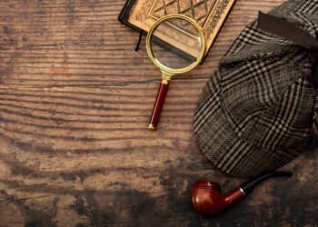 sherlock holmes detective hat, smoking pipe, retro magnifying glass and old book isolated on wood table top with copy space