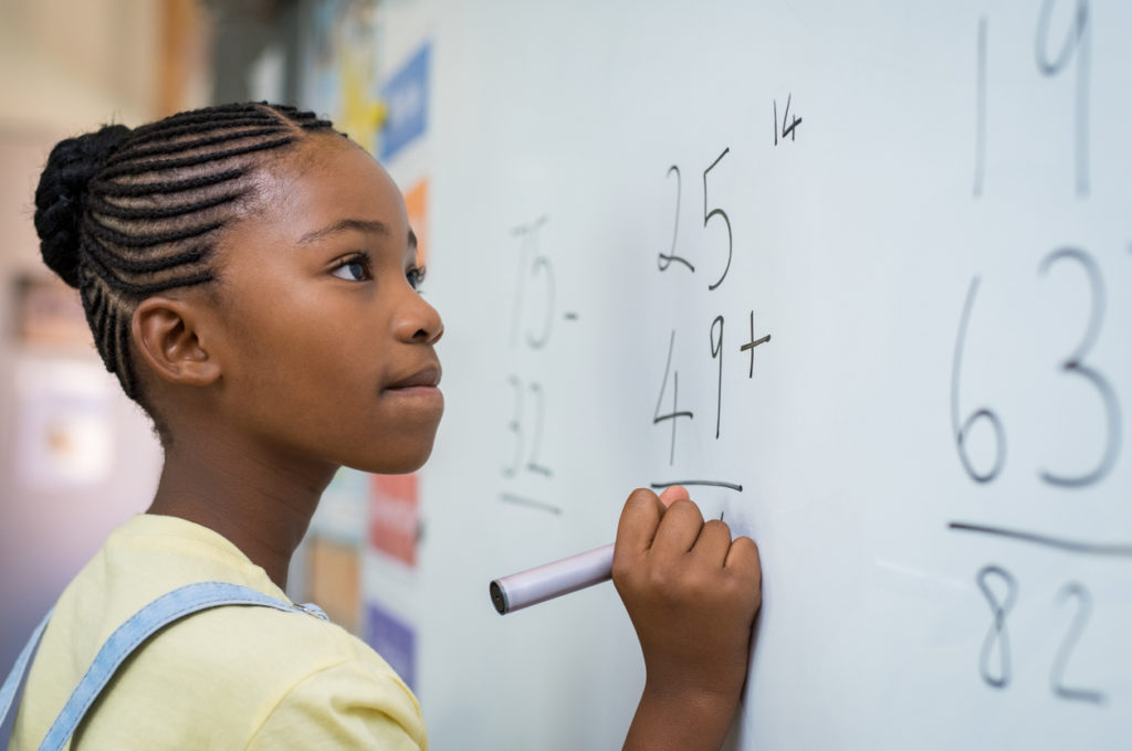 girl solving math problem at chalkboard