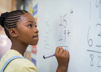 girl solving math problem at chalkboard