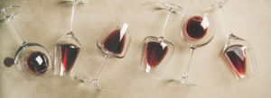 Flat-lay of red wine in glasses over grey concrete background, top view, copy space, wide composition.