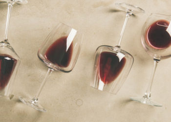 Flat-lay of red wine in glasses over grey concrete background, top view, copy space, wide composition.