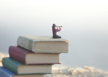 miniature person atop a stack of books