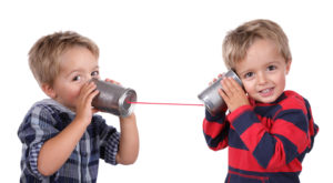 Two young boys using tin cans and a string as a telephone