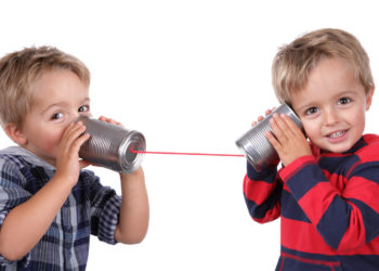 Two young boys using tin cans and a string as a telephone
