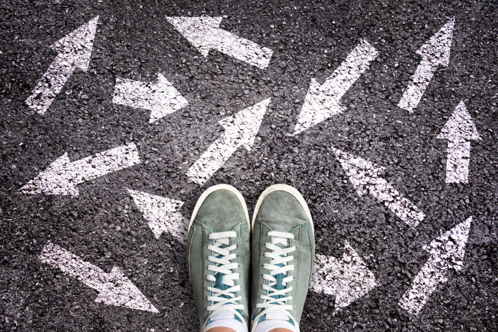 Sneaker shoes and arrows pointing in different directions on asphalt ground