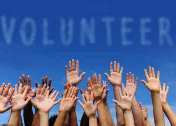 volunteer group raising hands against blue sky