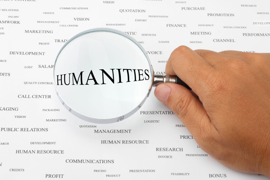 Hand holding a magnifying glass over the word "Humanities"