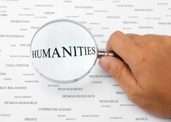 Hand holding a magnifying glass over the word "Humanities"