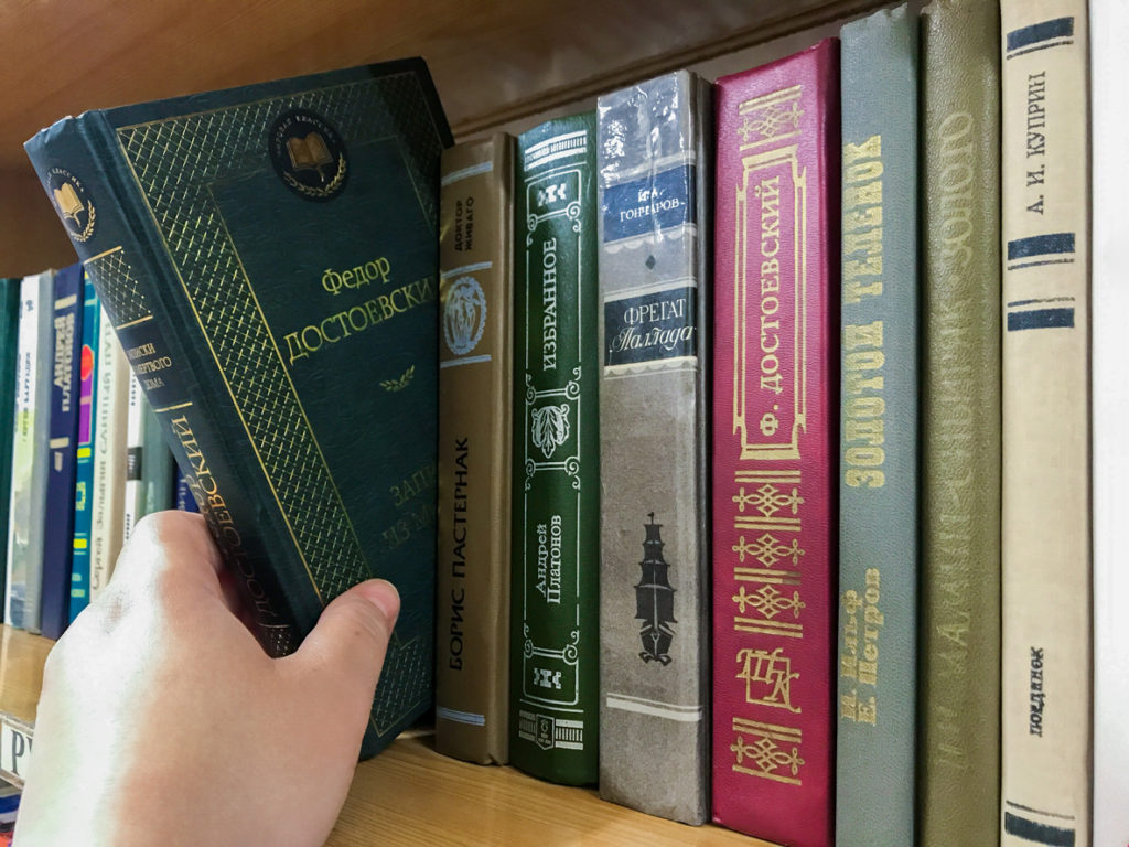 Close-up of a bookshelf with books by Russian writers. Hand pulls out Dostoevsky's book.
