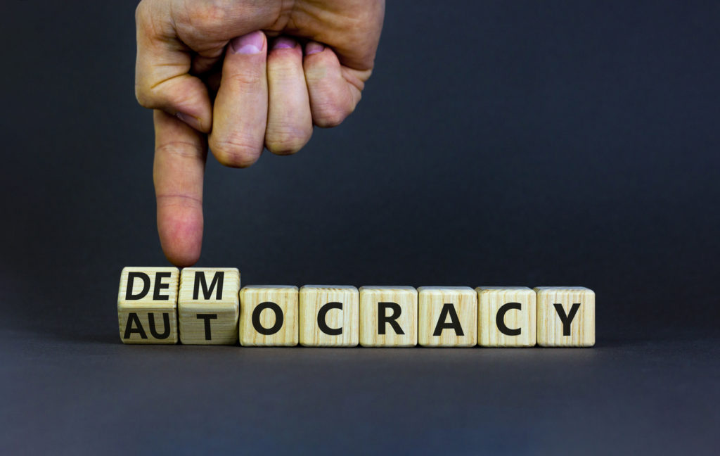 hand turning wooden cubes with letters from democracy to autocracy