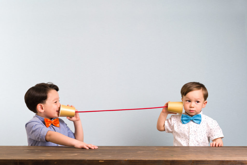 Two childeren are using paper cups as a telephone