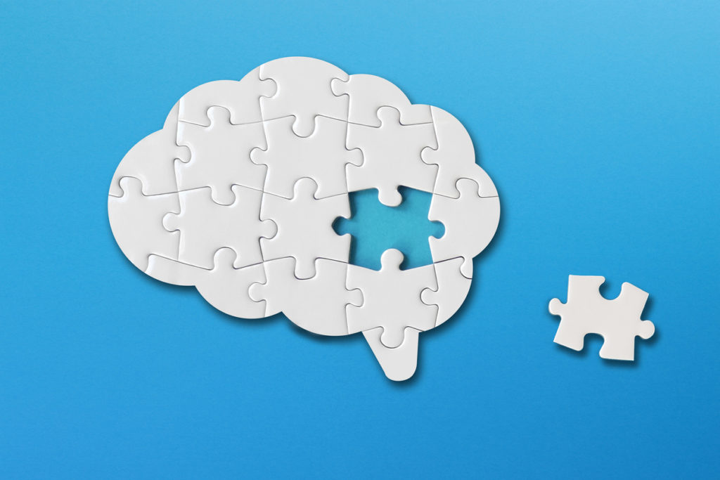 Brain shaped white jigsaw puzzle on blue background, with a missing piece of the brain puzzle