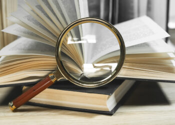Magnifying lens and open and closed books with turning pages on wooden table