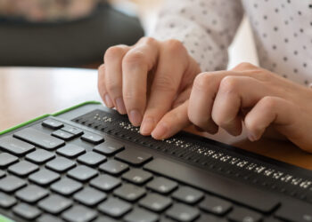 A person uses a computer with a Braille display and a computer keyboard