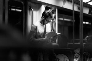 photograph of a man reading a book on a subway train
