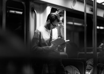 photograph of a man reading a book on a subway train