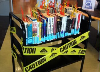 A cart of library books with "Caution" tape with banned books