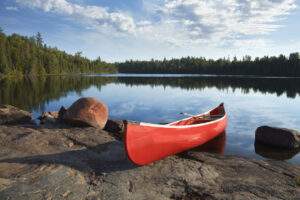 A red canoe rests on a rocky shore of a calm blue lake
