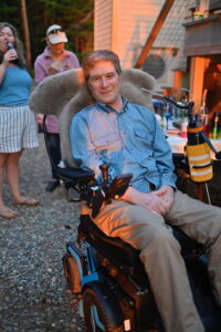 Bruce Rosenblum seated in a wheelchair at a party at sunset