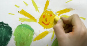 child's hand coloring a drawing of the sun