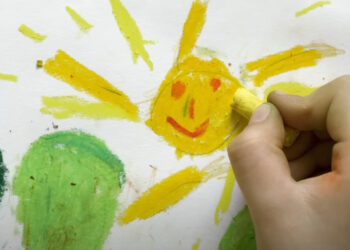 child's hand coloring a drawing of the sun