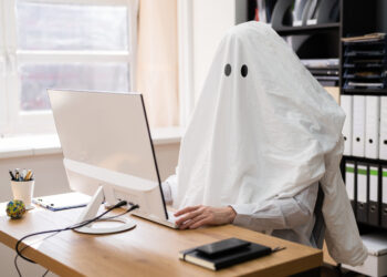 Person in ghost costume writing at a computer in an office