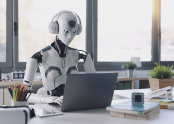 A humanoid robot works in an office on a laptop