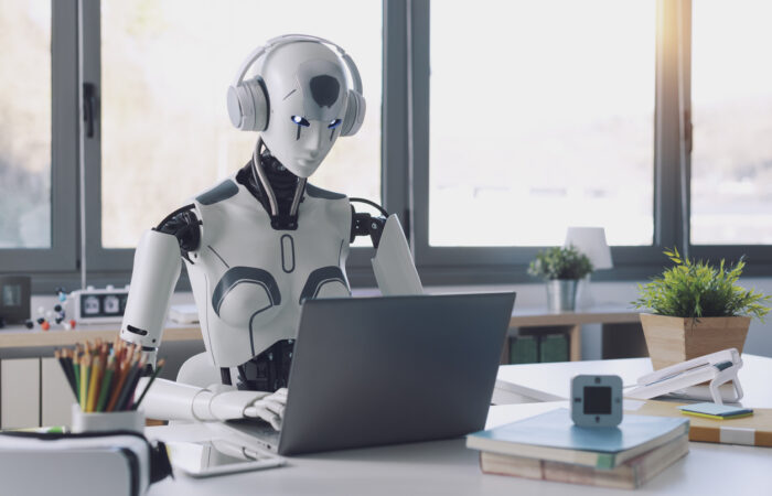 A humanoid robot works in an office on a laptop