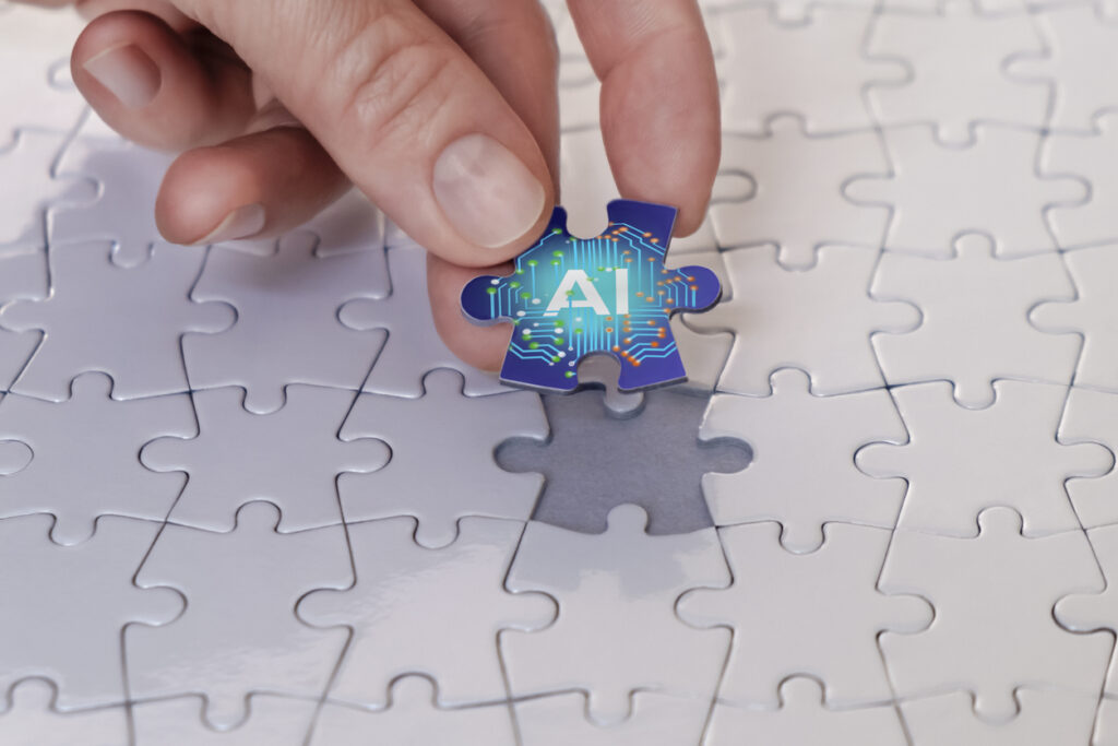 hand putting in last piece of puzzle, which is brightly colored and reads "AI"
