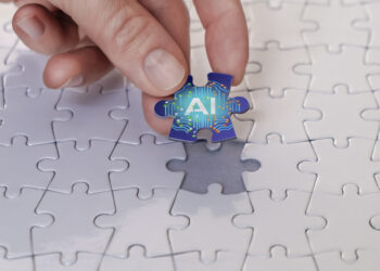 hand putting in last piece of puzzle, which is brightly colored and reads "AI"