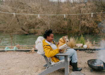 woman reading a book in her back yard by the fire pit with a dog