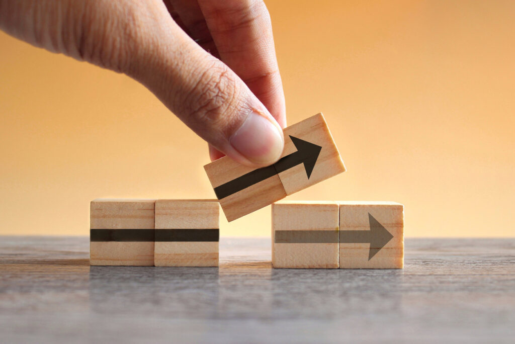 Hand holding wooden cubes with arrow icon, moving one out of position to point to a new direction