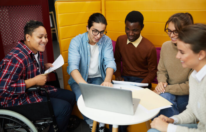 Multi-ethnic group of higher educational students using laptop while discussing team project during a gathering in a college library.