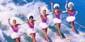 Photograph of the rock band The Go-Go's on water skis while dressed like beauty queens.