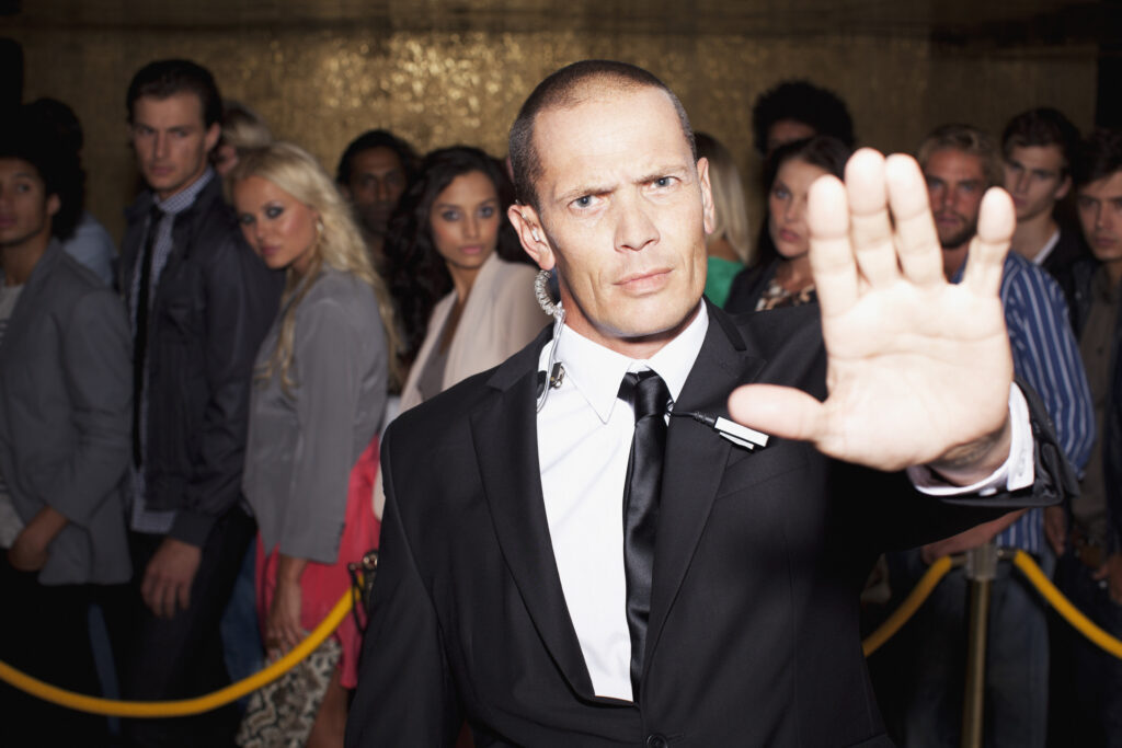 Stock photo of a stern bouncer with arm outstretched outside nightclub