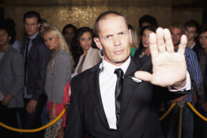 Stock photo of a stern bouncer with arm outstretched outside nightclub