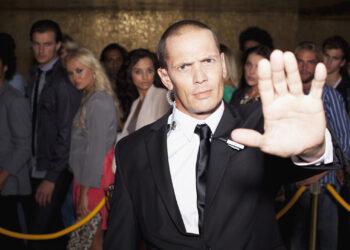 Stock photo of a stern bouncer with arm outstretched outside nightclub