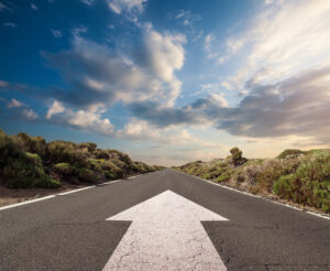 Blue sky with clouds and country road with white arrow pointing forward