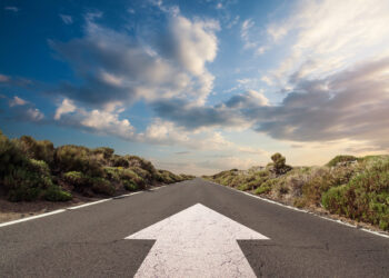 Blue sky with clouds and country road with white arrow pointing forward