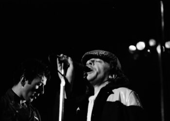 Ian Dury performing together with The Clash at the Tower Theater Show March 6, 1980. Image from John Coffey under CC BY license https://commons.wikimedia.org/wiki/File:IanDuryWithTheClash1980.jpg