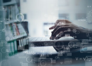 hands working on a laptop in front of a shelf full of books