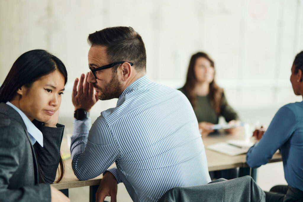 person whispering an aside to another person in a business setting