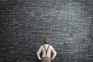 Man in hat and suspenders staring up at an equation filled chalkboard