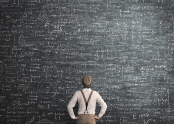 Man in hat and suspenders staring up at an equation filled chalkboard