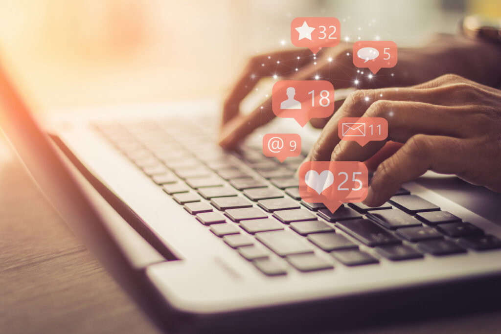 hands typing on a laptop keyboard with social media icons such as likes superimposed over the image